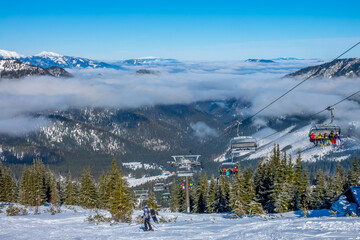 Skiers on the Chair Lift and Light Fog between Peaks