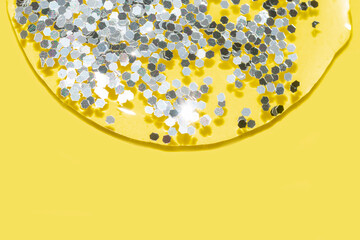 transparent liquid with silver glitter pouring over a pastel yellow background