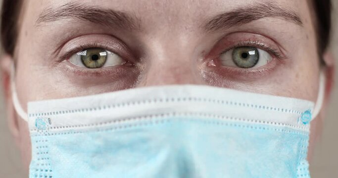 Close up young woman doctor in protective medical mask with gray eyes looks at the camera. COVID-19 Sars-cov-2 pandemic