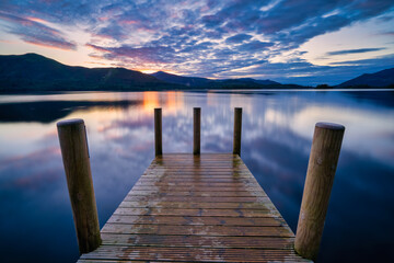 Vibrant sunset with dramatic clouds and wooden jetty at Derwentwater Lake in the Lake District, UK.