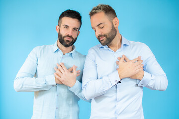 A young gay couple with peace gesture over blue background.