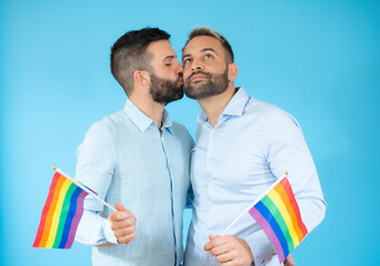 A young gay couple holding a flag over blue background.