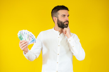 Photo of young man in casual shirt holding money in banknotes isolated over yellow background.