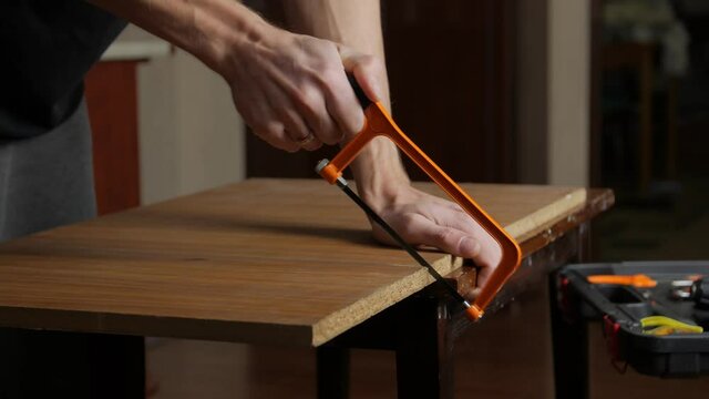 A man sawing a board handmade furniture chipboard evening home interior