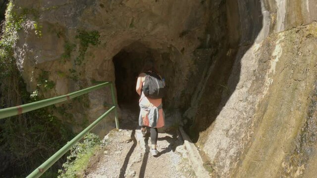 Cain, Spain - September 1, 2020: SLOW MOTION - Female hiking trough the Cares Route in the heart of Picos de Europa National Park, Spain. Narrow and impressive canyon between cliffs, bridges and caves