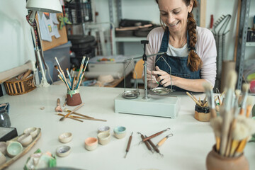 Caucasian woman mixing painting colors with a vintage balance inside her creative pottery studio - Focus on right hand