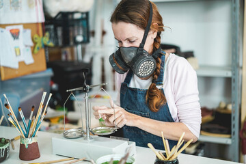 Caucasian artist woman mixing painting colors with a vintage balance inside her creative pottery studio while wearing gas mask - Art and workshop concept - Focus on her eye