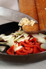 Adding minced garlic into skillet with red bell pepper and onion. Making Chicken and Egg Galette Series.