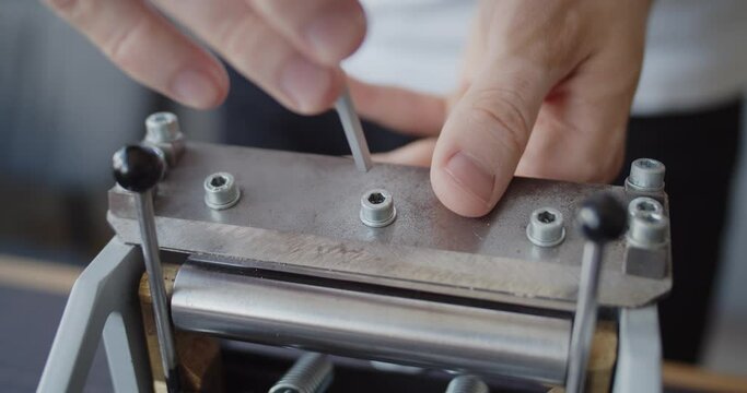 Making handmade leather belt. Leather worker tightens screws on a leather splitter after changing the blade. Close-up of hands.