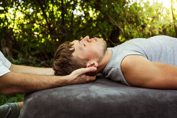 man doing osteopathic head massage to a guy in nature
