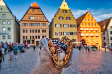 Obraz na płótnie Canvas Tourist concept of hand holding waffle covered with ice cream and fruits near the town square of Rothenburg in ob der Tauber in Germany