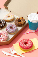 Set of yummy colorful donuts in paper box on pink background