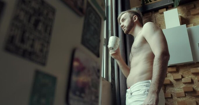 a man with a bare torso serves coffee at the apartment window. Slow motion.