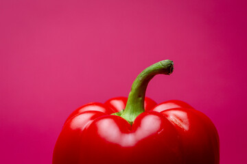 Clean purple colored frame with the top of a vibrant red Bell pepper or fresh paprika reflecting in studio lights and green stem sticking out