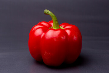 Colorful vibrant red Bell pepper or fresh paprika with green stem contrasted against a cool blueish smooth surface and background in studio lighting