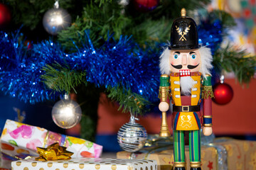 Wooden Nutcracker toy stands in front of decorated Christmas tree with gifts in the English House
