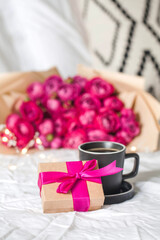 Coffee mug and a gift in bed on the background of a bouquet of flowers. Concept of Valentine's day, March 8.