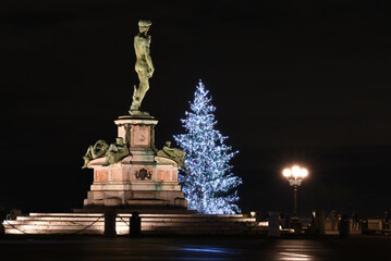 Bronze statue of David at Parco Michelangelo in Florence with illuminated Christmas tree in the background at evening. Florence, Italy.