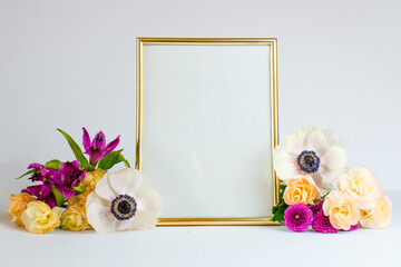 Gold empty frame with bouquet of spring flowers. Mock up frame and colorful flowers. Empty frame mock up for presentation design, modern art. Space for text. 