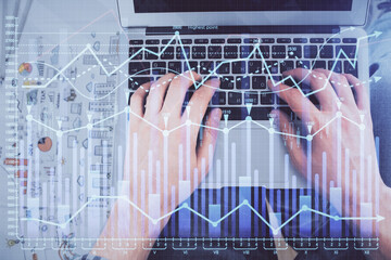 Double exposure of man's hands typing over laptop keyboard and forex chart hologram drawing. Top...