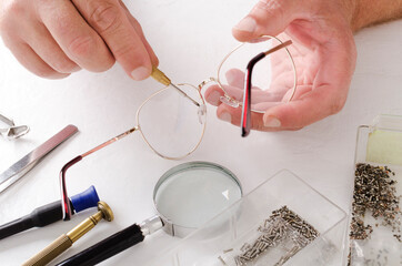 Closeup of male hands who fixing eyeglasses.Optical fixing kit, lens, screws and glasses on the...