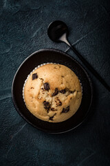 Fresh chocolate chip muffin on black plate. Top view