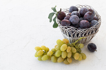 Just picked plums and grapes in wicker basket on white backdrop.
