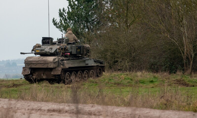 british army scimitar FV107 vehicle during a firepower demonstration on salisbury plain, reversing in to a copse for camouflage