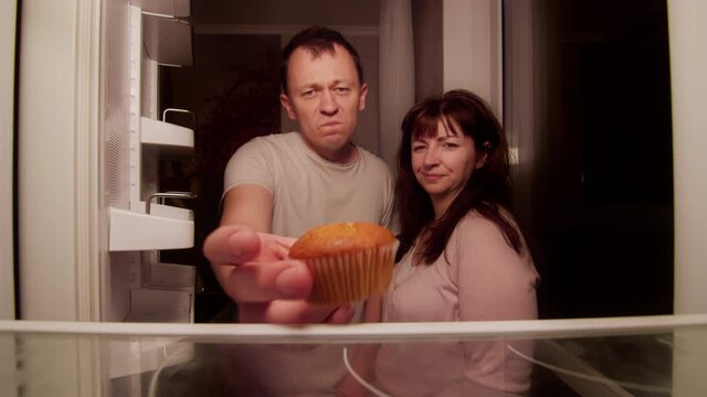 Married couple opens the refrigerator at night and finds there one spoiled cupcake