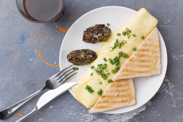 Omelette with fried champignon mushrooms, cheese and toasted bread and cup of coffee on gray table