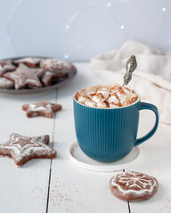 Hot cocoa in turquoise cup with marshmallows and gingerbread cookies on a white table