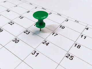 Green pushpin stuck into calendar, event reminder