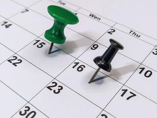 Green and black pushpins stuck into calendar, event reminder