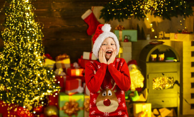 Santa brought me gifts. December tradition. Favorite day of year. Child happy excited near christmas tree. Merry christmas. Happy childhood concept. Kid wear santa hat and christmas sweater