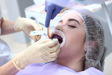 Professional teeth cleaning. The dentist applies a purple gel to the patient's teeth before...