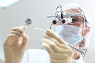 A dentist with binocular glasses holds a mirror in his hand. My hands are out of focus. Prevention...