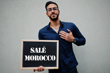 Arab man wear blue shirt and eyeglasses hold board with Sale Morocco inscription. Largest cities in islamic world concept.