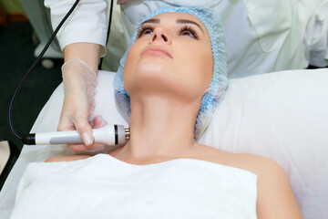 Naklejka premium A young woman is lying on the RF-lifting procedure for face skin tightening and face contour correction. Close-up.