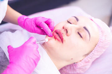 Doctor cosmetologist makes lip augmentation procedure to a beautiful woman in a beauty salon....