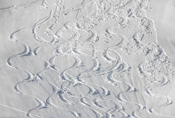 Wavy Ski tracks in deep snow on snowy mountain slope. White Winter sport background.