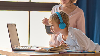 mom helping young son with laptop to do homework. Young woman teaching little boy to use the computer. baby sitter teaching little child girl use laptop application.
