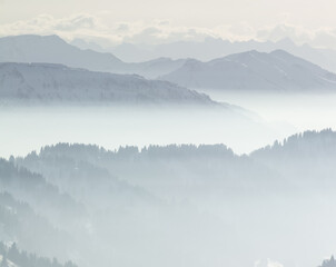 Snow Mountains in low lying inversion valley fog. Silhouettes of foggy Mountains and trees. Scenic snowy winter landscape. View from Stuiben Swiss Alps, Allgau, Bavaria, Germany.