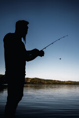 Silhouette of a young fisherman with his fishing rod - Silhouette of a young man casting his fishing rod during a sunset fishing session in front of the river.