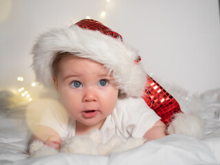 Adorable baby girl in Santa hat lying on the bed