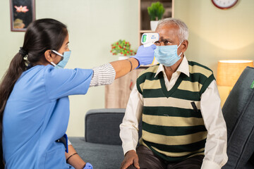 doctor or nurse checking temperature of old sick man using infrared thermometer at hospital while both worn face mask due to coronavirus covid-19 safety measures