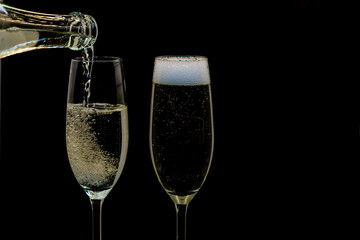Pouring gold champagne into glass, a lot of bubbles insidde, isolated on black background, white froth on the top