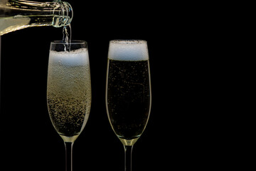 Pouring gold champagne into glass, a lot of bubbles insidde, isolated on black background, white froth on the top