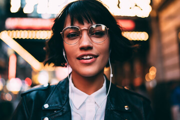 Portrait of beautiful hipster girl in stylish spectacles enjoying favourite music and time for walk...