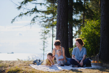 Homosexual lesbian family with two children, a son and a daughter. Two moms and kids at an outdoor picnic. Forest and sea.