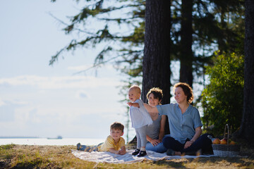 Homosexual lesbian family with two children, a son and a daughter. Two moms and kids at an outdoor picnic. Forest and sea.